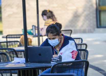 masked female student working on laptop outside on campus