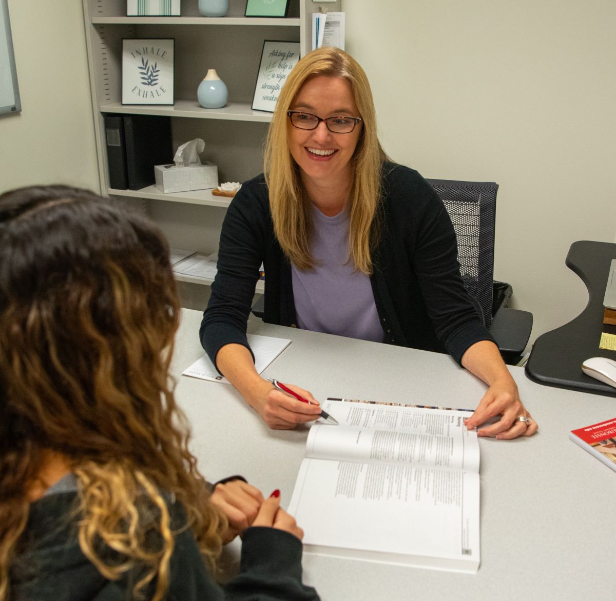 Internship staff member helping student in her office, showing her a document on her desk