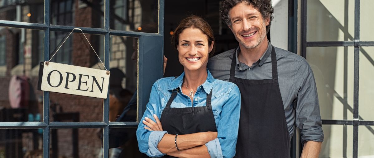 Two small business owners in front of store with open sign
