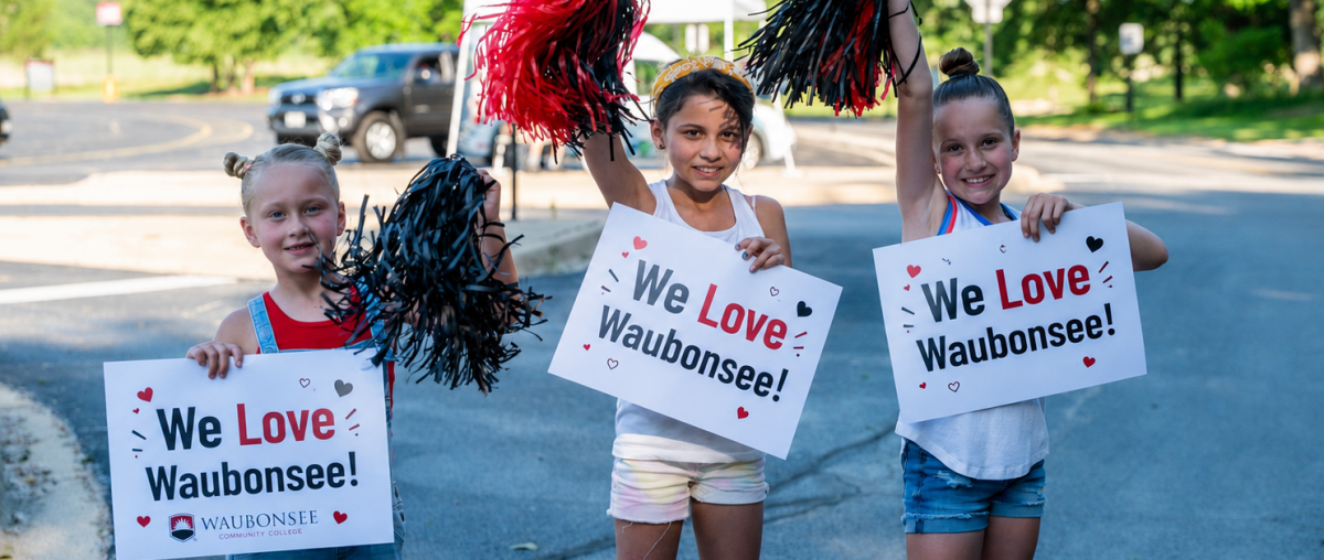 Three young people stand holding pom poms and signs that say "We Love Waubonsee"