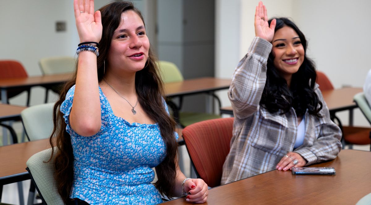 Two students in classroom raising hand
