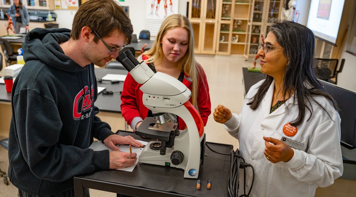 Dr. Sheela Vemu, Associate Professor of Biology, instructing two students on microscope