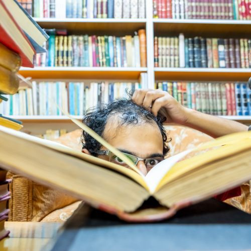 Man scratching head behind stack of library books