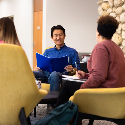 Three adult students sitting at a table in front of Dickson Center fireplace.