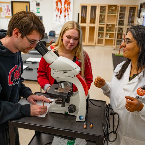 Dr. Sheela Vemu, Associate Professor of Biology, instructing two students on microscope