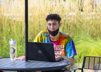 masked student working on laptop outside on campus
