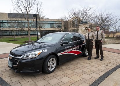 Two campus cadets standing next to police car