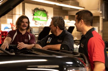 two automotive students with instructor working on truck engine