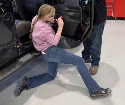 young female student working on vehicle door panel in TEC class