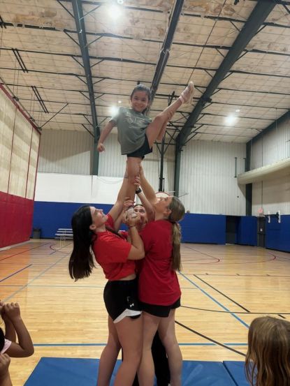 3 female cheerleaders holding up a child cheerleader