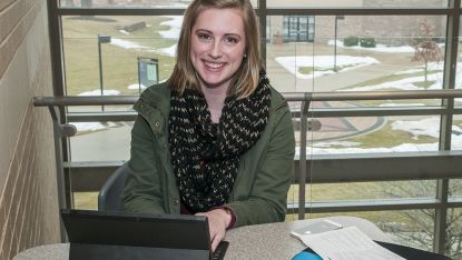 female student with laptop sitting infront of big window inside s