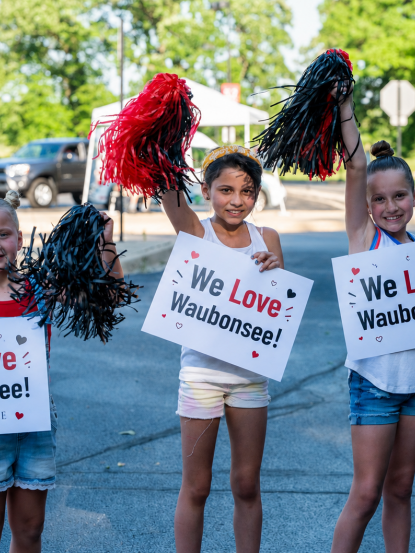 Three young people stand holding pom poms and signs that say "We Love Waubonsee"