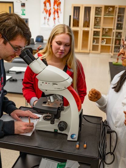 Dr. Sheela Vemu, Associate Professor of Biology, instructing two students on microscope