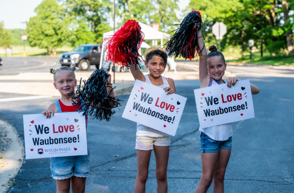 Three young people stand holding pom poms and signs that say "We Love Waubonsee"
