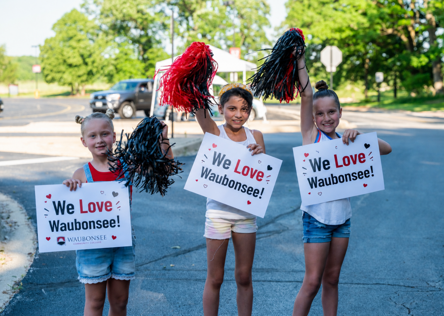 Three young people stand holding pom poms and signs that say "We Love Waubonsee"