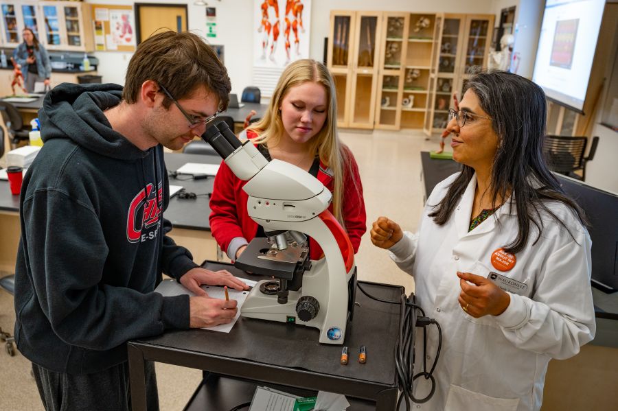 Dr. Sheela Vemu, Associate Professor of Biology, instructing two students on microscope